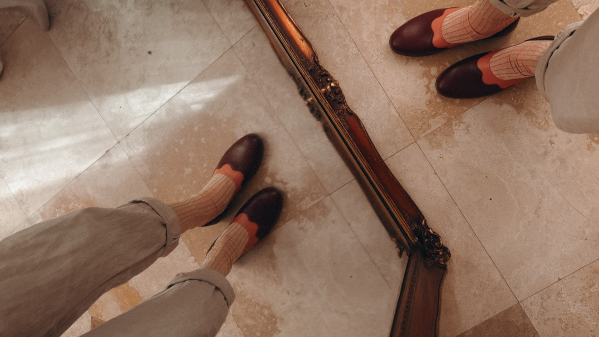 Person wearing brown shoes with orange accents and beige pants, standing on a tiled floor.