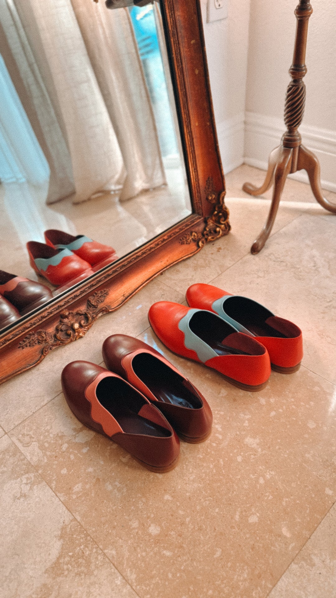 Pair of red and brown shoes on a marble floor with a large mirror reflecting the room.